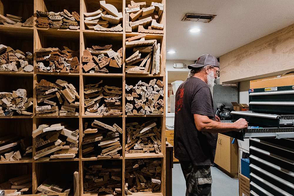 Woodlane team member in office pulling open a file cabinet, with a tall shelf stocked full of wood moldings.