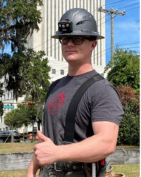 Caleb Millican, Installation team member, posing humorously outside with safety gear and a thumbs up.